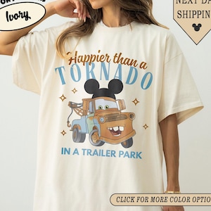 K&ouml;nnte beinhalten: Elfenbeinfarbenes T-Shirt mit dem Text "Happier than a Tornado in a Trailer Park" und einem Cartoon-Bild von Mater aus dem Film Cars. Das Shirt hat eine lockere Passform und ist aus weichem Material.