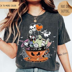 K&ouml;nnte beinhalten: Pfefferfarbenes T-Shirt mit einem Halloween-Motiv. Das Design zeigt Charaktere aus Nightmare Before Christmas in einer Jack-o'-Lantern-Tasse, mit Luftballons und Spinnweben. Das T-Shirt hat einen Vintage-Look.