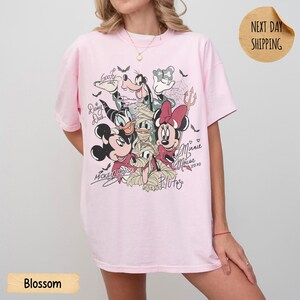 Peut inclure: T-shirt rose clair avec un motif de personnages Disney d&eacute;guis&eacute;s pour Halloween. Mickey, Minnie, Donald, Dingo et Pluto sont repr&eacute;sent&eacute;s. Le t-shirt porte les noms "Mickey Mouse", "Minnie Mouse" et "Pluto".