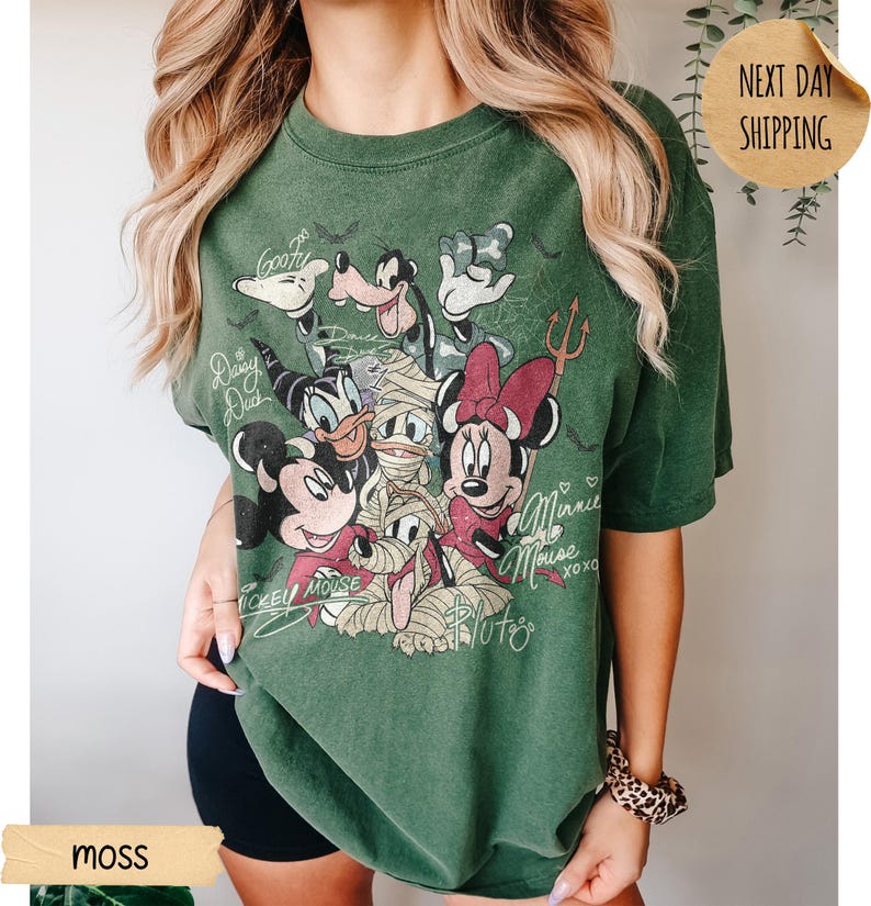Peut inclure: T-shirt vert mousse avec un motif vintage de personnages Disney, dont Mickey Mouse, Minnie Mouse, Donald Duck, Dingo et Pluto. Le motif comprend les inscriptions "Mickey Mouse", "Minnie Mouse" et "Pluto".