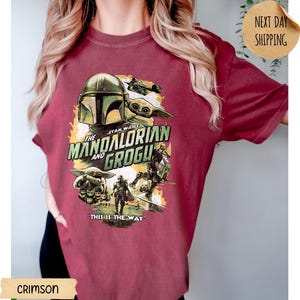 Pu&ograve; includere: T-shirt cremisi con una grafica della serie Star Wars, "The Mandalorian and Grogu". Il design include il casco del Mandaloriano, Grogu e la frase "This is the Way". La maglietta ha un girocollo e maniche corte.
