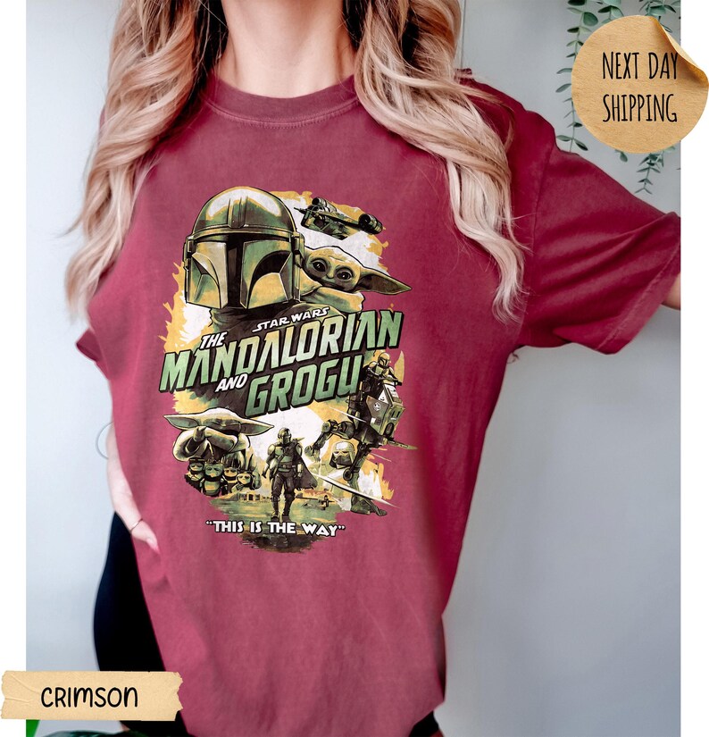 Pu&ograve; includere: T-shirt cremisi con una grafica della serie Star Wars, "The Mandalorian and Grogu". Il design include il casco del Mandaloriano, Grogu e la frase "This is the Way". La maglietta ha un girocollo e maniche corte.