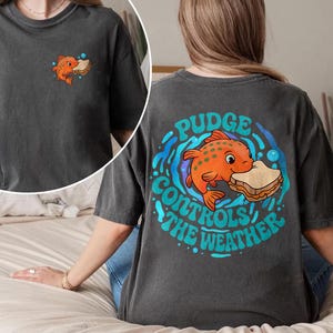 May include: Dark grey t-shirt with a cartoon orange fish holding a sandwich, and the text "Pudge Controls the Weather" on the back. A smaller version of the fish and sandwich graphic is on the front.