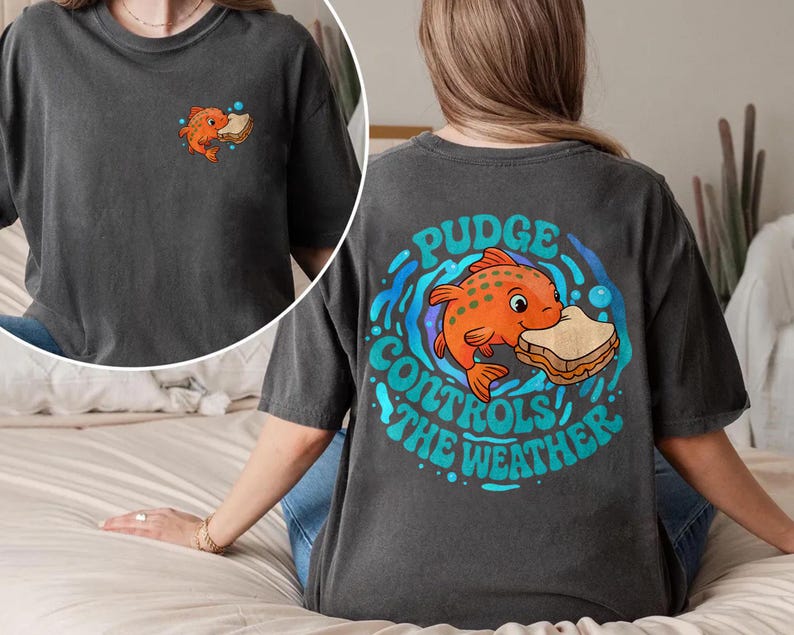 May include: Dark grey t-shirt with a cartoon orange fish holding a sandwich, and the text "Pudge Controls the Weather" on the back. A smaller version of the fish and sandwich graphic is on the front.