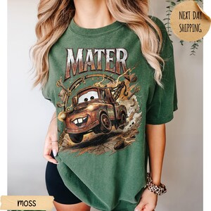 May include: Green t-shirt with a graphic of Mater from the Cars film. The design features the word "MATER" above the cartoon tow truck. The shirt is a moss green colour.