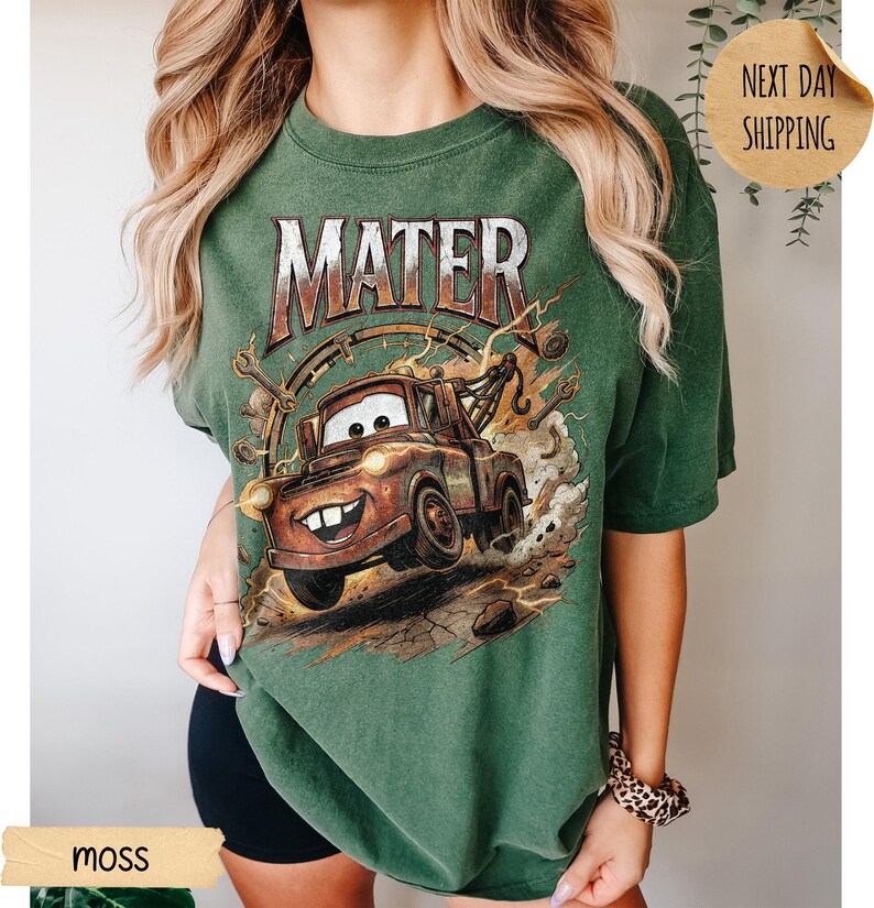 May include: Green t-shirt with a graphic of Mater from the Cars film. The design features the word "MATER" above the cartoon tow truck. The shirt is a moss green colour.
