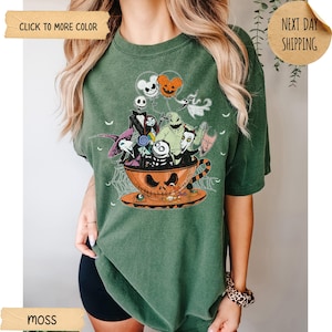 K&ouml;nnte beinhalten: Moosgr&uuml;nes T-Shirt mit einem Halloween-Motiv. Das Design zeigt Charaktere aus "Nightmare Before Christmas" in einer Jack-o'-Lantern-Tasse. Das Shirt hat einen Rundhalsausschnitt und kurze &Auml;rmel.