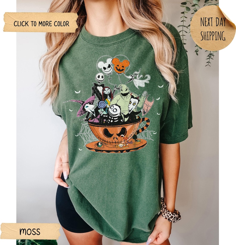 K&ouml;nnte beinhalten: Moosgr&uuml;nes T-Shirt mit einem Halloween-Motiv. Das Design zeigt Charaktere aus "Nightmare Before Christmas" in einer Jack-o'-Lantern-Tasse. Das Shirt hat einen Rundhalsausschnitt und kurze &Auml;rmel.