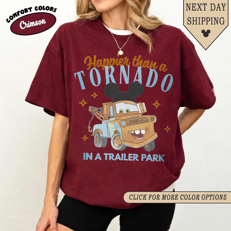 K&ouml;nnte beinhalten: Karmesinrotes T-Shirt mit dem Text "Happier than a TORNADO IN A TRAILER PARK" und einem Cartoon-Abschleppwagen mit Mickey Mouse-Ohren. Das Shirt hat auch die W&ouml;rter "COMFORT COLORS" und "Crimson" darauf.