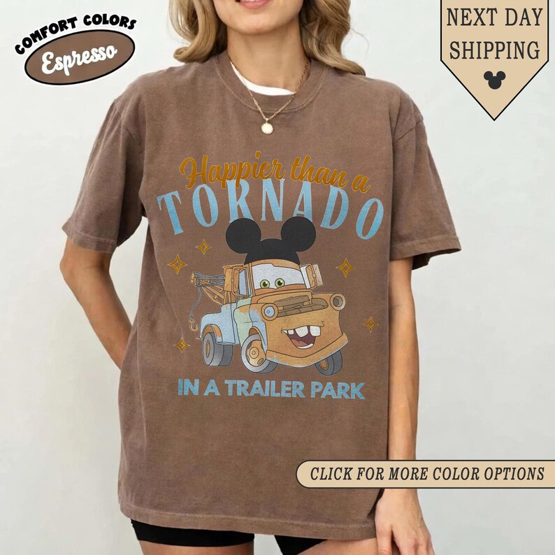 K&ouml;nnte beinhalten: Braunes T-Shirt mit dem Text "Happier than a TORNADO in a trailer park" und einem Cartoon-Abschleppwagen-Design. Das Shirt hat auch den Text "Comfort Colors Espresso" und "Next Day Shipping".