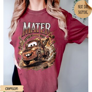 May include: Crimson t-shirt with a cartoon image of Mater from the film Cars. The word "MATER" is printed above the image in a distressed font. The graphic includes a tow truck, lightning bolts, and a smiling face, set against a background.