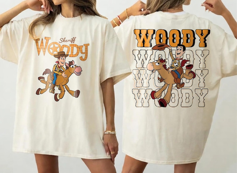 May include: Cream-colored t-shirt featuring a cartoon image of Sheriff Woody riding a horse. The front of the shirt has the text "Sheriff Woody" in orange and brown. The back of the shirt has the word "Woody" repeated multiple times.