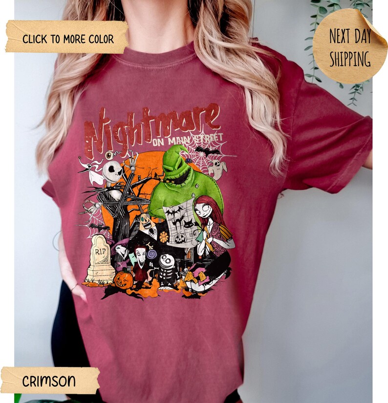 May include: A crimson short-sleeve t-shirt featuring a graphic print with the text Nightmare on Main Street. The design includes characters like Jack Skellington, Sally, and Oogie Boogie, along with a tombstone, a pumpkin, and a spider web.