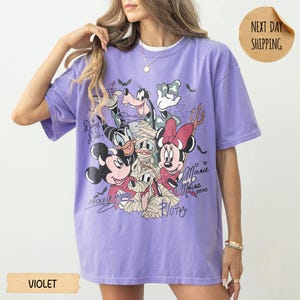Peut inclure: T-shirt violet &agrave; manches courtes avec un motif de personnages Disney en costumes d'Halloween. Le design comprend Mickey, Minnie, Donald, Dingo et Pluto. Le t-shirt porte les inscriptions "Mickey Mouse" et "Minnie Mouse".