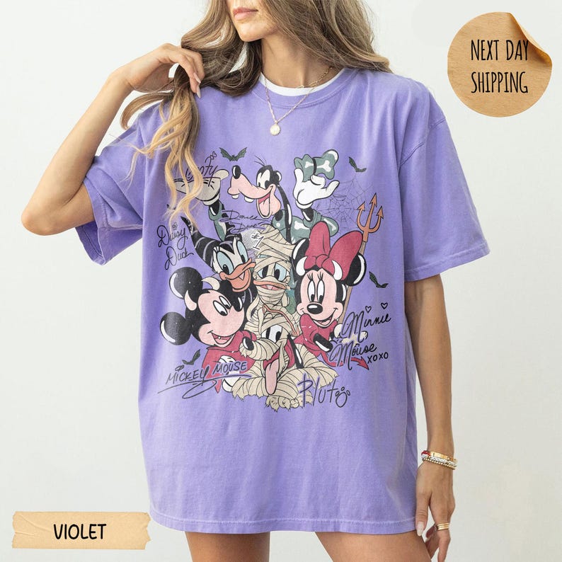 Peut inclure: T-shirt violet &agrave; manches courtes avec un motif de personnages Disney en costumes d'Halloween. Le design comprend Mickey, Minnie, Donald, Dingo et Pluto. Le t-shirt porte les inscriptions "Mickey Mouse" et "Minnie Mouse".