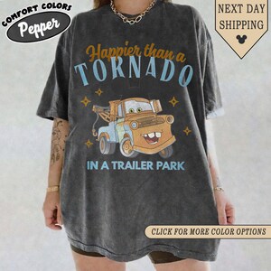 K&ouml;nnte beinhalten: Dunkelgraues T-Shirt mit einem Cartoon-Bild von Hook aus dem Film Cars. Das Shirt tr&auml;gt den Text "Happier than a TORNADO IN A TRAILER PARK" in Blau und Orange. Das Shirt hat auch die Logos Comfort Colors und Pepper.