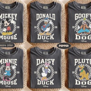 May include: Six dark gray t-shirts featuring Disney characters Mickey Mouse, Donald Duck, Goofy, Minnie Mouse, Daisy Duck, and Pluto. Each shirt has a character graphic with the character's name, the year 1928, and the Disney logo.