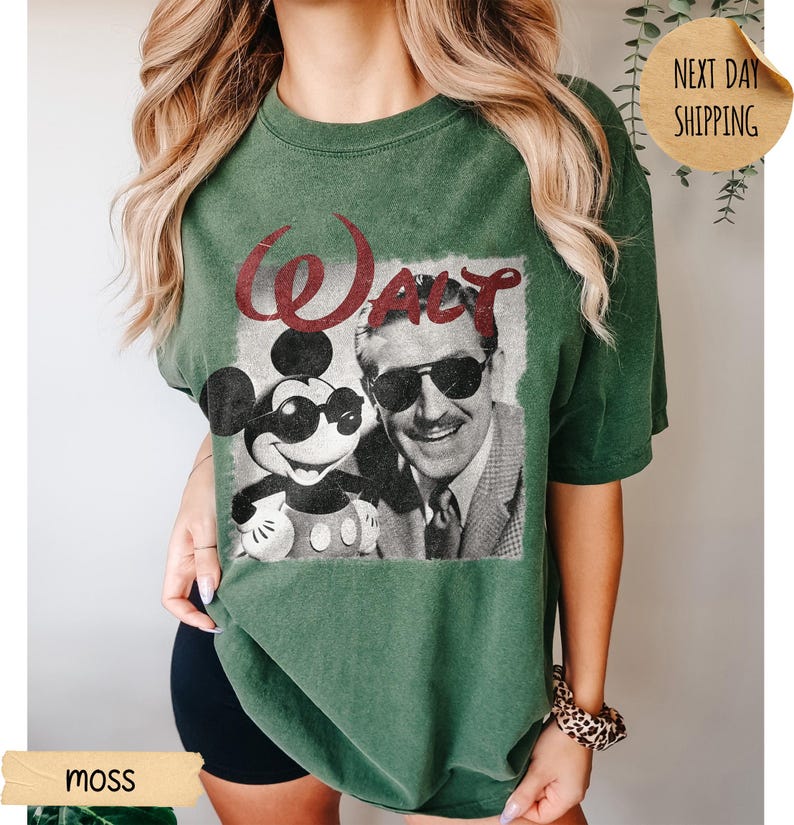 May include: Moss green t-shirt featuring a graphic of Mickey Mouse wearing sunglasses and Walt Disney. The word "Walt" is printed in red above the image. The shirt is a relaxed fit.