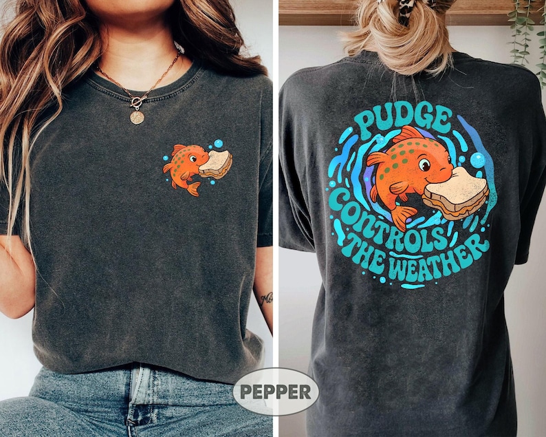May include: Charcoal grey t-shirt with a cartoon orange fish and sandwich graphic. The front has a small fish design, and the back features a larger design with the text "Pudge Controls the Weather" in a circular arrangement.