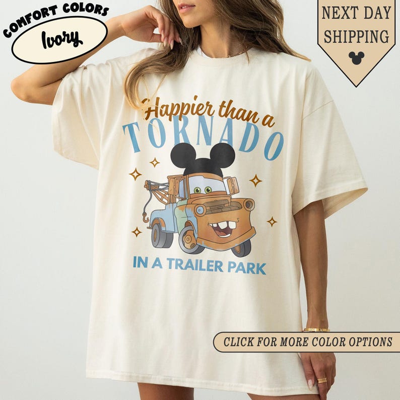 K&ouml;nnte beinhalten: Elfenbeinfarbenes T-Shirt mit dem Text "Happier than a Tornado in a Trailer Park" und einem Cartoon-Bild von Mater aus dem Film Cars. Das Shirt hat eine lockere Passform und ist aus weichem Material.