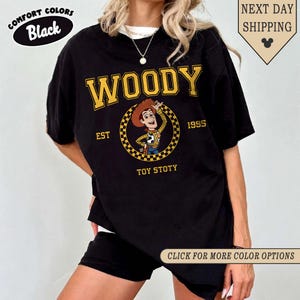 Puede incluir: Camiseta negra con un gr&aacute;fico de Woody. El dise&ntilde;o presenta la palabra "WOODY" en amarillo, una imagen de dibujos animados de Woody y el texto "EST 1995 TOY STOTY". La camiseta tambi&eacute;n tiene las palabras "COMFORT COLORS Black" y "CLICK FOR MORE COLOR OPTIONS".