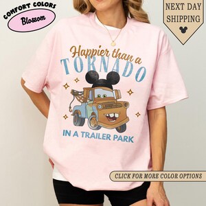 K&ouml;nnte beinhalten: Hellrosa T-Shirt mit einem Cartoon-Abschleppwagen mit Mickey Mouse Ohren und dem Text "Happier than a Tornado in a Trailer Park". Das Shirt hat auch den Text "Comfort Colors Blossom".