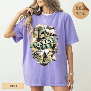 Pu&ograve; includere: T-shirt viola con grafica di Star Wars con The Mandalorian e Grogu. Il design include l'elmo del Mandaloriano, Grogu e il testo "The Mandalorian and Grogu" e "This is the Way".