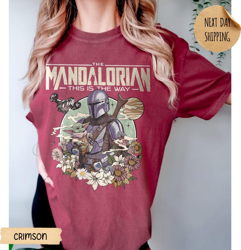 May include: Crimson t-shirt featuring a graphic of The Mandalorian and Grogu surrounded by flowers. The text on the shirt reads "THE MANDALORIAN - THIS IS THE WAY". The design includes a spaceship and a planet.