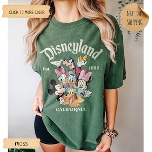 Op de afbeelding: Mosgroen T-shirt met een Disneyland-afbeelding met Mickey Mouse en vrienden. De tekst "Disneyland Est 1955 California" staat op de voorkant. Het shirt heeft korte mouwen.