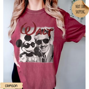May include: Crimson-colored t-shirt featuring a vintage graphic of Mickey Mouse and Walt Disney wearing sunglasses. The word "Walt" is printed above the image in a stylized font. The shirt has a classic crew neck and short sleeves.