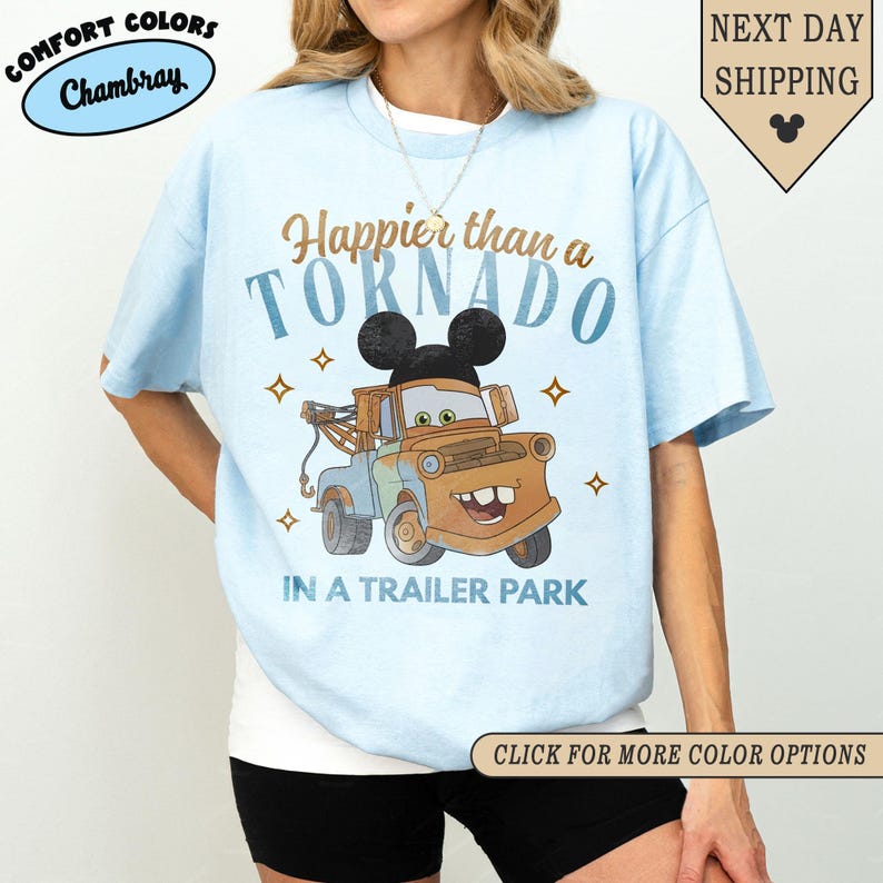 K&ouml;nnte beinhalten: Hellblaues T-Shirt mit einem Cartoon-Abschleppwagen mit Mickey Mouse-Ohren und dem Text "Happier than a Tornado in a Trailer Park". Auf dem Shirt steht auch "Comfort Colors Chambray".