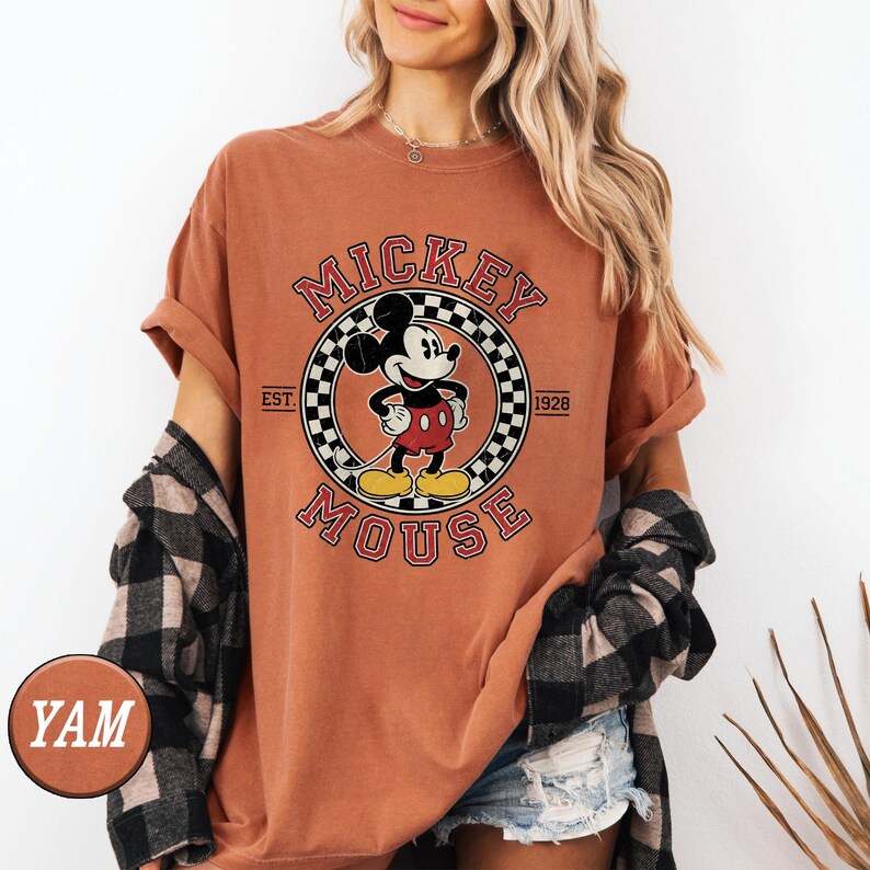 Puede incluir: Camiseta de color terracota con un gr&aacute;fico cl&aacute;sico de Mickey Mouse. El dise&ntilde;o incluye un emblema circular con Mickey Mouse, las palabras "Mickey Mouse" y "Est. 1928". La camiseta tiene mangas cortas y un corte relajado.