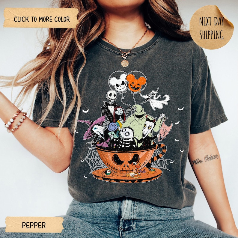 K&ouml;nnte beinhalten: Pfefferfarbenes T-Shirt mit einem Halloween-Motiv. Das Design zeigt Charaktere aus Nightmare Before Christmas in einer Jack-o'-Lantern-Tasse, mit Luftballons und Spinnweben. Das T-Shirt hat einen Vintage-Look.