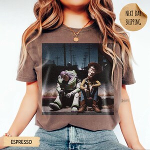Pode incluir: Camiseta cor caf&eacute; com estampa desgastada de Buzz Lightyear e Woody de Toy Story. Os personagens s&atilde;o retratados sentados em uma cal&ccedil;ada &agrave; noite. A camiseta tem um visual vintage e desgastado.