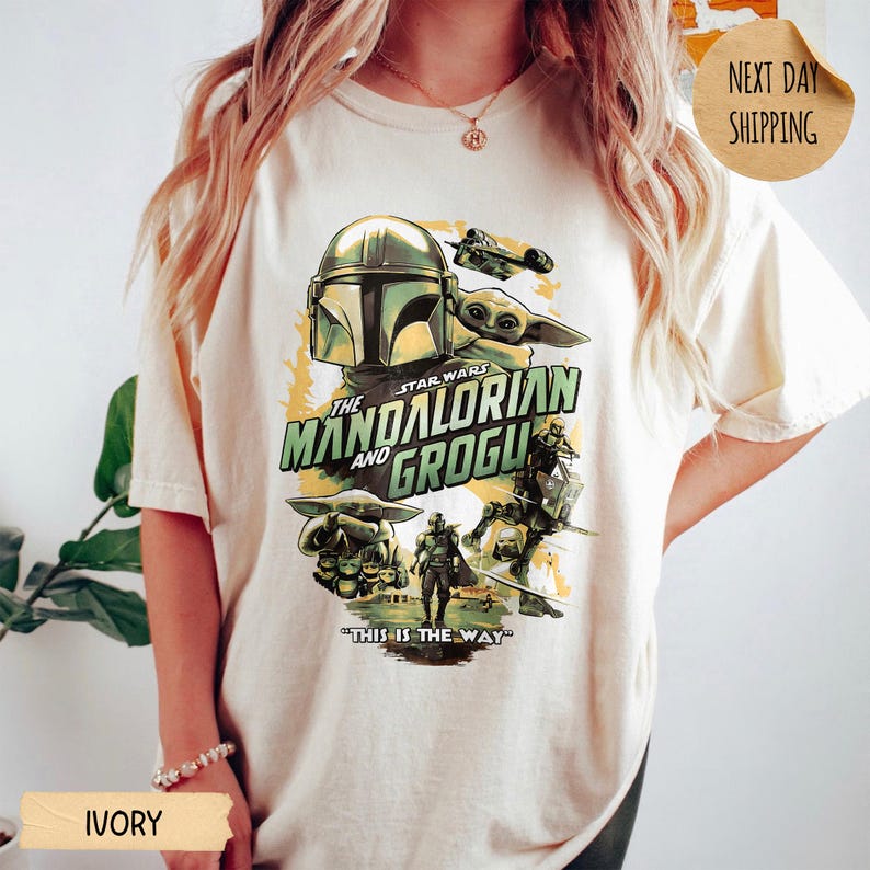 Pu&ograve; includere: T-shirt color avorio con grafica di Star Wars con The Mandalorian e Grogu. Il design include immagini del Mandaloriano, Grogu e un'astronave, con la frase "THIS IS THE WAY".