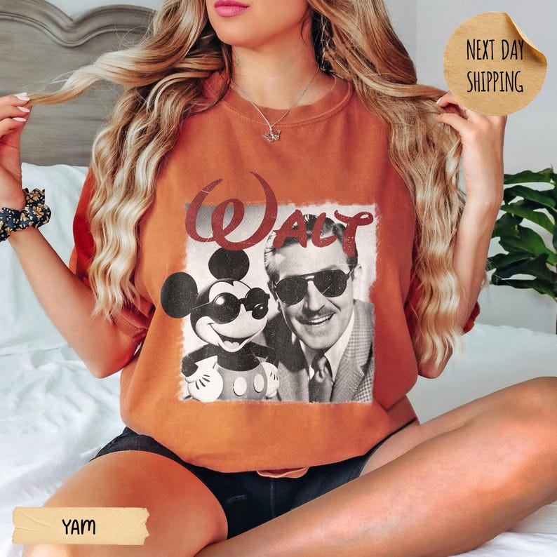 May include: Burnt orange t-shirt featuring a vintage graphic of Mickey Mouse wearing sunglasses and Walt Disney. The word "Walt" is printed above the image in a red, distressed font. The shirt has a relaxed fit.