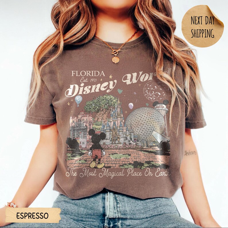 May include: Espresso-colored t-shirt featuring a vintage-style graphic of Disney World in Florida. The design includes Mickey Mouse, the Epcot ball, and the text "Florida Disney World" and "The Most Magical Place On Earth."