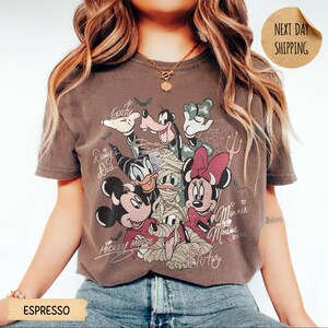 Peut inclure: T-shirt couleur expresso avec un motif de personnages Disney en costumes d'Halloween. Mickey Mouse, Minnie Mouse, Donald Duck, Daisy Duck, Dingo et Pluto sont repr&eacute;sent&eacute;s. Le t-shirt a un aspect vintage et vieilli.