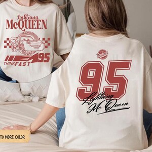 May include: Cream-colored t-shirt featuring Lightning McQueen graphics. The front displays the character's image with text, while the back showcases a large "95" and the character's name. A fun, casual tee.