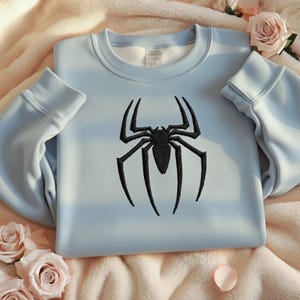 Puede incluir: Sudadera azul claro con un dise&ntilde;o de ara&ntilde;a negra bordada. La sudadera de cuello redondo est&aacute; hecha de un material suave y tiene pu&ntilde;os y dobladillo acanalados. El dise&ntilde;o de la ara&ntilde;a est&aacute; bordado en la parte delantera.