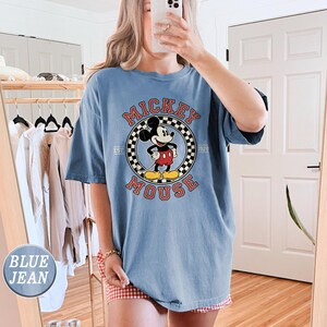 Puede incluir: Camiseta azul claro con un dise&ntilde;o de Mickey Mouse en un c&iacute;rculo, con las palabras "Mickey Mouse" y "Est. 1928". La camiseta es de corte holgado y tiene mangas cortas.