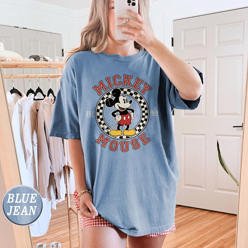 Puede incluir: Camiseta azul claro con un dise&ntilde;o de Mickey Mouse en un c&iacute;rculo, con las palabras "Mickey Mouse" y "Est. 1928". La camiseta es de corte holgado y tiene mangas cortas.
