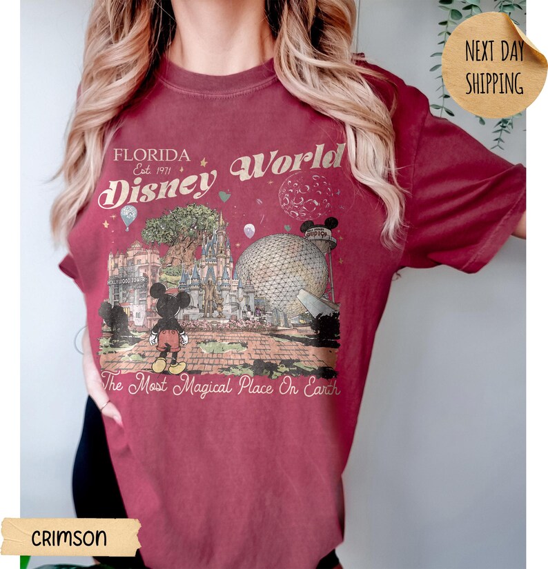 May include: Crimson t-shirt featuring a vintage-style graphic of Disney World in Florida. The design includes Mickey Mouse, the park's landmarks, and the text "Florida Disney World Est. 1971" and "The Most Magical Place On Earth."
