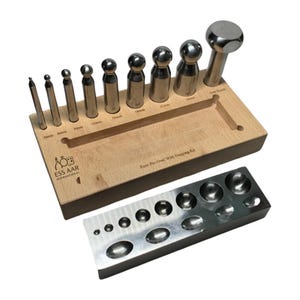 Puede incluir: Un kit para hacer joyas con una base de madera y herramientas de metal, incluyendo punzones y un bloque de embutido. Las herramientas están etiquetadas con medidas en milímetros. El kit incluye el texto "ESS AAR INTERNATIONAL".