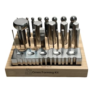 May include: A metal jewellery forming kit with various shapes and sizes of metal tools. The tools are arranged on a wooden base with the text "Multi Block" and "Omen Forming Kit". The kit includes cylindrical, ball-shaped, and flat-ended tools.