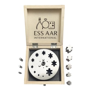 Pode incluir: Uma caixa de madeira aberta com um conjunto de ferramentas para fazer joias. O texto "ESS AAR INTERNATIONAL" está na tampa. O conjunto inclui uma placa de metal circular com várias formas, pequenas peças de metal e peças em forma de quebra-cabeça.