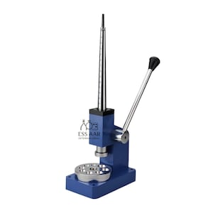 May include: A blue metal ring sizing machine with a silver lever and a measuring rod. The machine has a round base with multiple holes and the text "ESS AAR INTERNATIONAL".