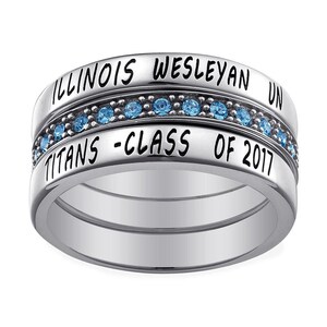 May include: A silver ring with three bands. The top band reads "ILLINOIS WESLEYAN UN", the middle band has blue gemstones, and the bottom band says "TITANS - CLASS OF 2017".