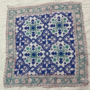 May include: Square white cloth with a blue and teal floral pattern. The center design features a repeating pattern of blue and teal floral motifs. The border has a floral design in teal and pink.