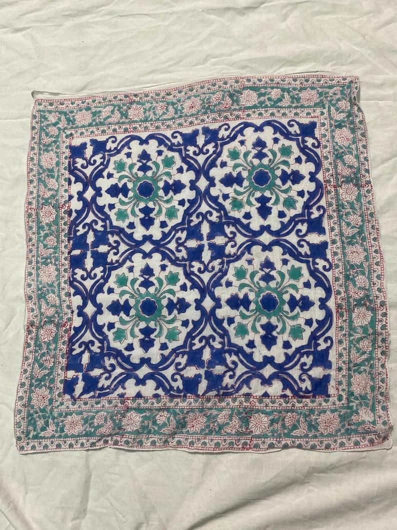 May include: Square white cloth with a blue and teal floral pattern. The center design features a repeating pattern of blue and teal floral motifs. The border has a floral design in teal and pink.